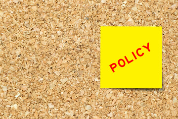 Yellow note paper with word policy on cork board background with copy space