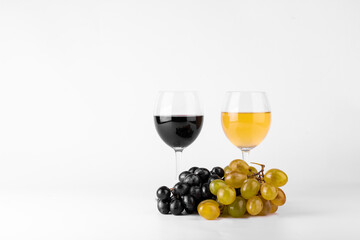 Red and white wine in glasses with red and white grapes on white background.