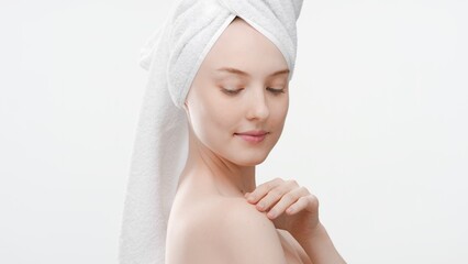 Young cute fit Caucasian woman with a towel on her hair touches her shoulder on white background | Body care concept