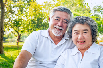Obraz premium A cheerful elderly couple wearing white shirts, sitting close together in a sunny park, enjoying a beautiful day outdoors. 