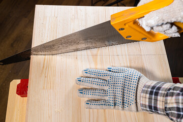Fototapeta na wymiar above view of carpenter hands sawing wooden board with hand saw on workbench at home