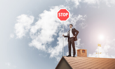 Caucasian businessman on brick house roof showing stop road sign
