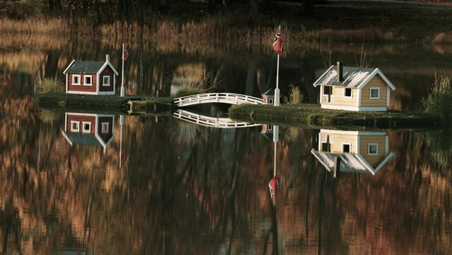 An idyllic scene. Toy houses in the middle of the lake reflected in the mirrorlike still water. Bright autumn foliage in the background.