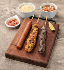 Meat, chicken and pork sausage skewers over wooden board with farofa and vinaigrette