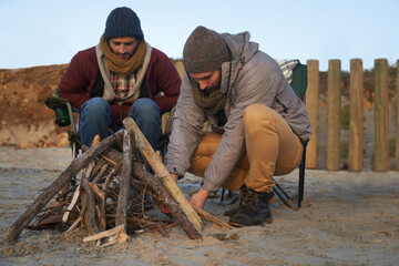 Lets get this a blazing. Two young men building a fire on the beach.