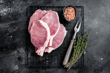 Raw pork cutlet chop steak for fry on pan with herbs. Black background. Top view