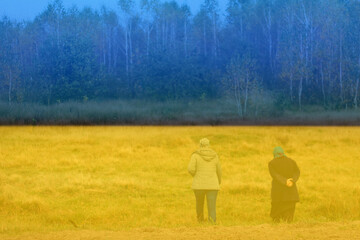 War refuge. Defocus rear view of two woman on a walk in autumn nature. Fall background. Beautiful park landscape. Two women walking along the road in the autumn forest. Back view. Out of focus