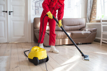 a cleaner in a red uniform cleans the floor with the help of steam coming out of the nozzle of the...