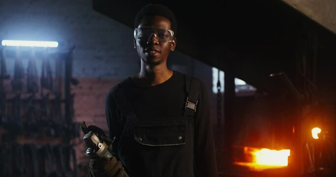 A young blacksmith of African American appearance in goggles looks at the camera