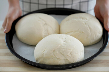 Woman showing three homemade loaves of bread in baking tray ready to be baked