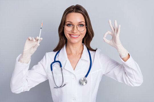 Photo of young woman pediatrician hold syringe show okey symbol good recommend isolated over grey color background