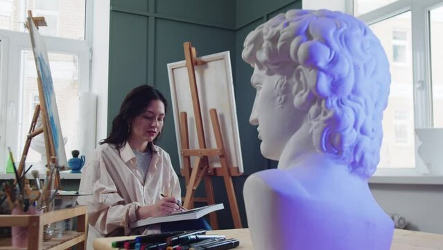 A woman artist sketches from the marble bust in an art studio