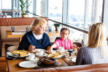 childhood and people concept - happy grandmother and little girl with spoon eating at outdoor cafe or restaurant