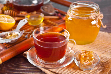Cup of herbal tea with flowers, honey in jar, teapot and and various dried herbs on the tray.