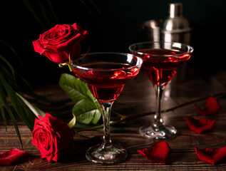 Delicious refreshing beverage drink red cocktail with red rose and petals on wooden table. Romantic, Valentines day concept.