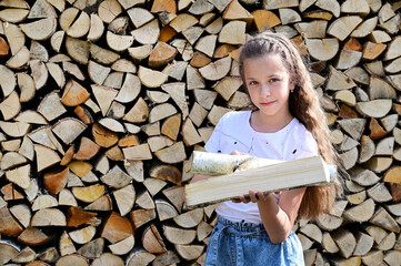 beautiful girl with long hair in white T-shirt on background of pile of firewood. Сoncept of harvesting firewood for winter. Firewood for fireplace. Close-up