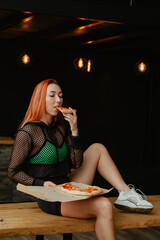 Sporty woman with red hair in sports clothes eat pizza in kitchen at home.