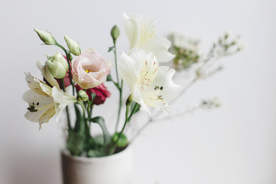 Stylish bouquet in ceramic vase at window, moody image. Beautiful fresh flowers, manuka, alstroemeria, eustoma, eucalyptus floral arrangement. Spring modern bouquet close up