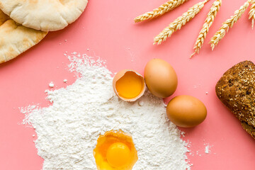 Baking background with eggs, flour and bread on pink table. Top view.