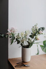 Fototapeta na wymiar Stylish bouquet in ceramic vase on wooden windowsill. Beautiful fresh flowers and scissors on wooden background, floral arrangement. Spring modern bouquet