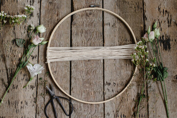 Making stylish spring wreath with beautiful fresh flowers. Wooden hoop, thread, scissors, and...