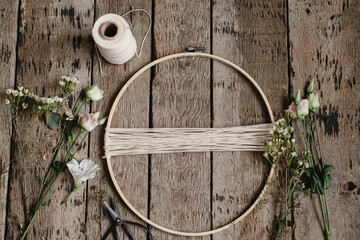 Making stylish spring wreath with beautiful fresh flowers flat lay. Wooden hoop, thread, scissors,...