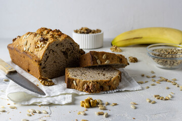 Banana bread with seeds and walnuts on a light napkin. Cutters in a white vase and bananas in the background. Seeds scattered on the table