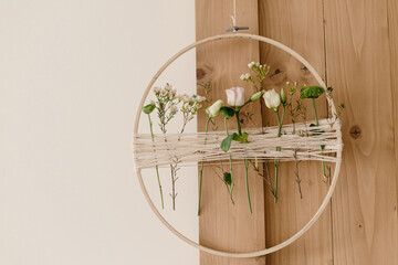 Stylish spring boho wreath with beautiful fresh flowers. Wooden hoop with flowers and thread on wooden door. Modern and creative floral handmade decor