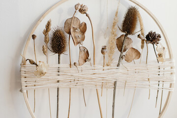 Stylish boho autumn wreath with dry flowers. Wooden hoop, thread and dry herbs on white wall...