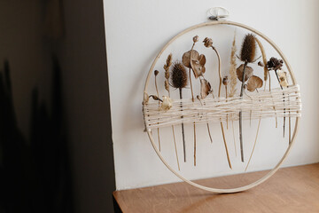 Stylish boho autumn wreath with dry flowers. Wooden hoop, thread and dry herbs on background of room. Modern floral arrangement and creative handmade decor © sonyachny