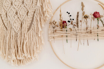Stylish boho wreath with dry flowers and macrame hanging on white wall. Modern floral arrangement and creative handmade decor in modern boho room