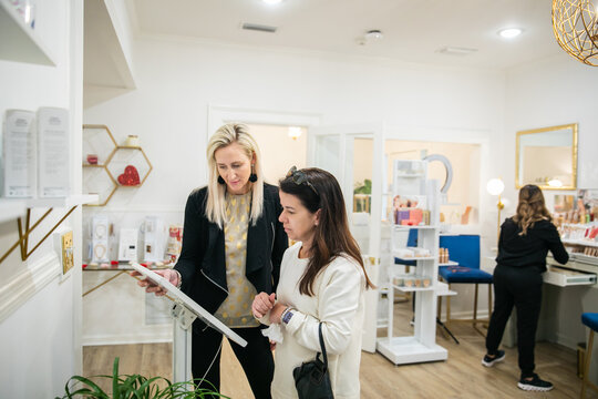 A woman helps another woman digitally check into a wellness spa for beauty treatments