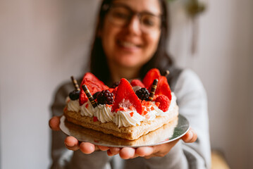 young smiling woman holding heart shaped cake with red ripe strawberries and fresh raspberries and blueberries. St. Valentine's Day, Mother's Day, or Birthday cake decorated with sugar hearts