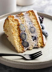 Piece of vanilla biscuit cake with cream and blueberries and blackberries close-up on a plate on a stone background. Gluten free healthy dessert.