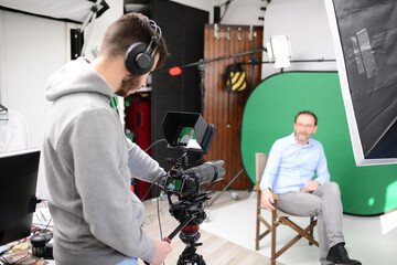 young man video camera operator making interview in professionnal broadcast tv movie studio film production with a green chromakey background