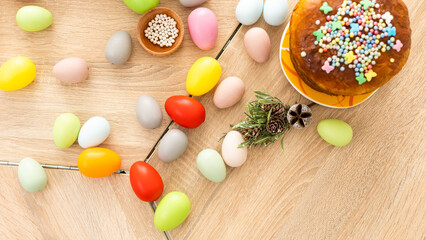 Easter cake with sprinkles, painted eggs and flowers on wooden table, flat lay. Space for text