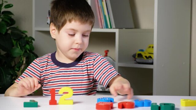 A boy of 4 years learns to count, arranges multi-colored figures of numbers