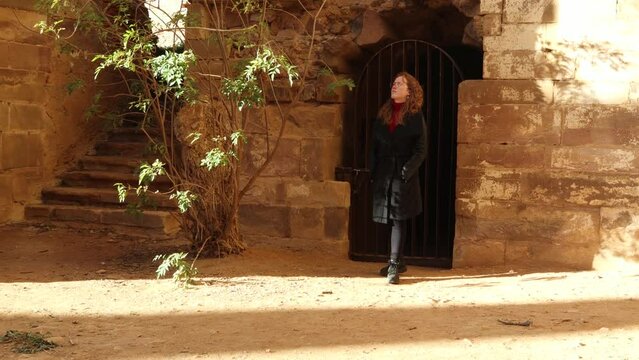 Young redhead girl admiring old gate on the ruins a monastery in Spain. XII-XIII century buiding of the christian monastic cluny order, female traveler. Woman exploring ancient ruins.