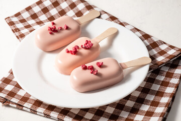 Popsicle in pink glaze, cake on a stick in a white plate. Cheesecake on a stick