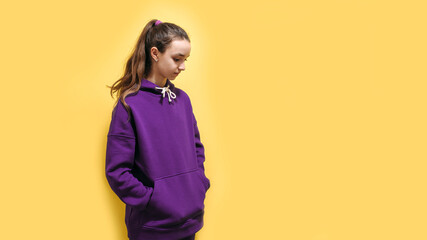 Cute teen girl in a purple hoodie. Kids hoodies mockup. Studio shot on yellow background.