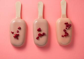 Three popsicle cakes in bright icing on a pink background, top view.