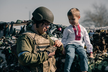Child boy sits on sandbags in checkpoint near Ukrainian territorial defense warrior.