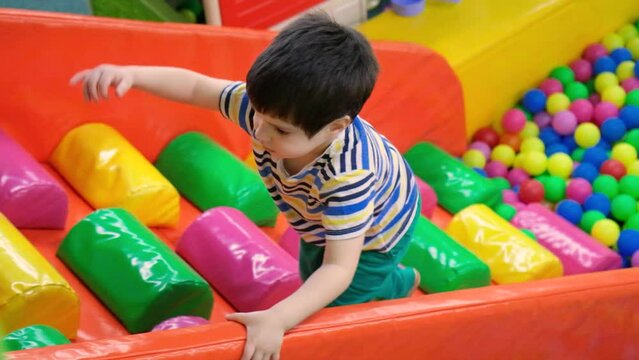 The boy climbs the slide on a colored soft staircase from the pool with soft balls, a playroom for children