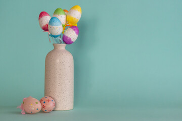 Bouquet of colorful Easter eggs placed in white vase with two pink eggs near against blue background 