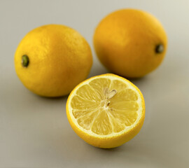 Dwie cytryny i jedna przekrojona na pół - połówka cytryny. Szare tło, obraz realistyczny. 