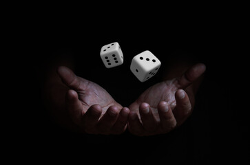 Human hand throwing two white dice in the air on a black background. game with dice, gambling...