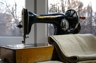 Hemp fabric and vintage sewing machine on the windowsill at home. Evening Golden Hour.	
