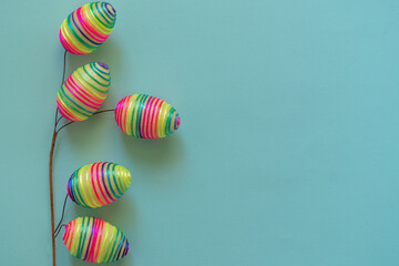 Top view mockup of multicolored rainbow striped eggs placed on branch on blue background 