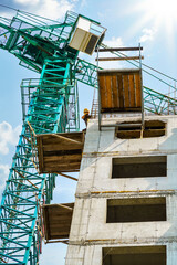 construction of a multi-storey residential building - a builder works at the top of the building, concrete frame, building materials and construction crane