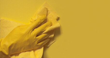 A hand in a yellow rubber glove with a rag on a yellow background.